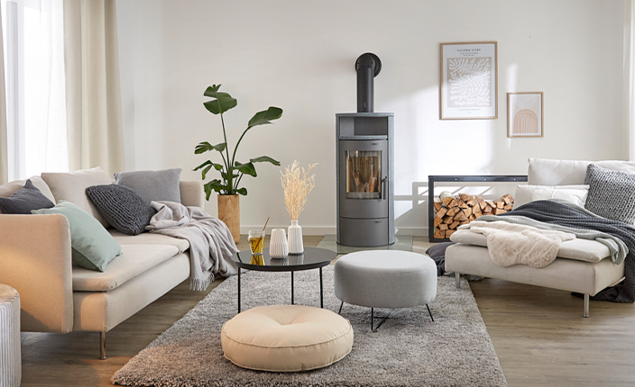 Gemütlich eingerichtetes Wohnzimmer mit Kaminofen, Holzvorrat, bequemen Sitzmöbeln und wohnlichen Accessoires.