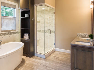 Ein modernes Badezimmer mit freistehender Badewanne, verglaster Eckdusche und einem Waschbecken mit Holzunterschrank. Die Wände sind hell gestrichen und der Boden ist mit großen Fliesen ausgelegt