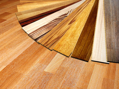 Verschiedene Laminat- und Vinylbodenmuster in Holzoptik liegen fächerförmig auf einem Holzboden aus