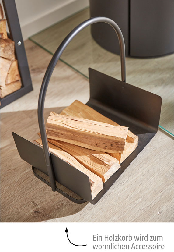 Schwarzer Metall-Holzkorb mit Kaminholz auf hellem Holzboden vor Kaminofen.
