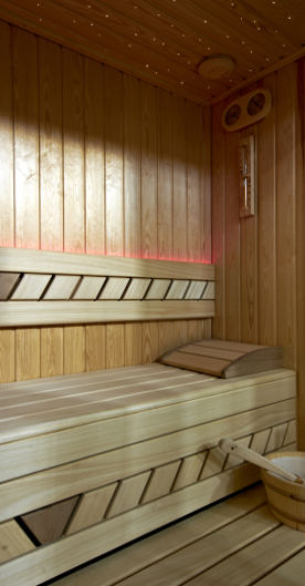 Holzsauna mit Liegefläche, Kopfkissen, Eimer und dezenter Beleuchtung.