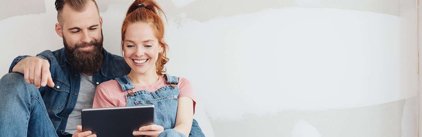 Eine Frau und ein Mann sitzen mit dem Rücken an einer Wand und schauen gemeinsam auf ein Tablet