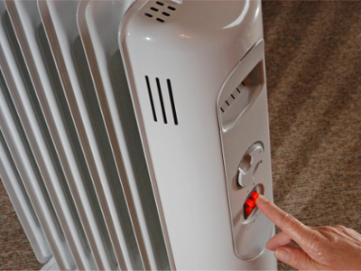 Eine Person schaltet einen weißen Radiator mit Kippschalter auf einem Teppichboden ein