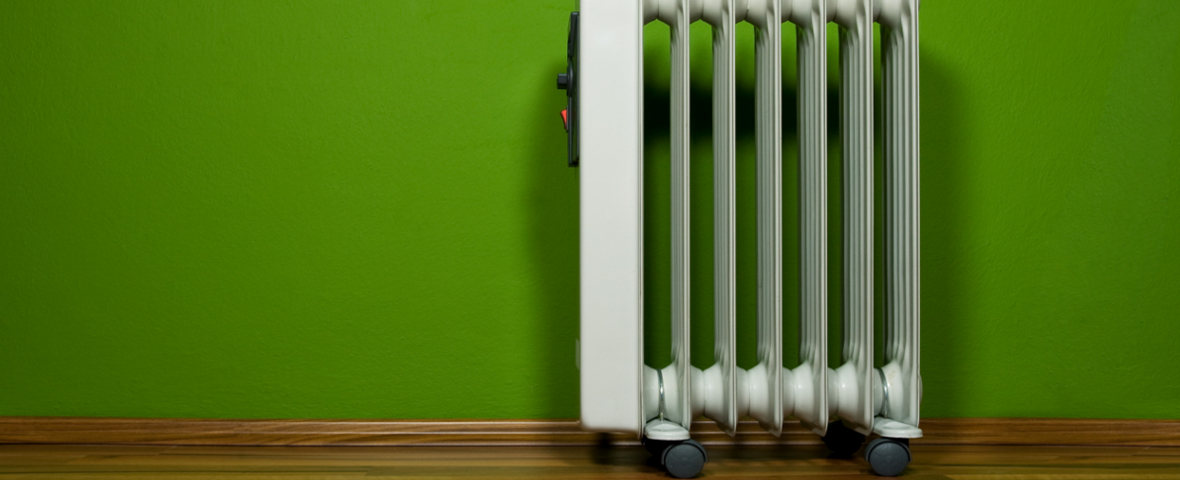 Ein weißer, mobiler Radiator steht vor einer grünen Wand auf einem Holzboden und sorgt für zusätzliche Raumwärme