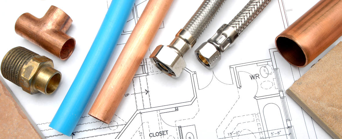 Verschiedene Sanitärmaterialien wie Kupferrohre, ein flexibler Metallschlauch und ein Kunststoffrohr liegen auf einem Badezimmergrundriss