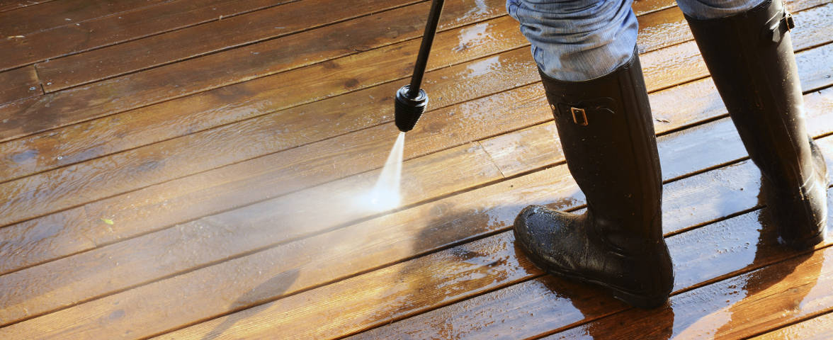 Person reinigt eine Holzterrasse mit einem Hochdruckreiniger.