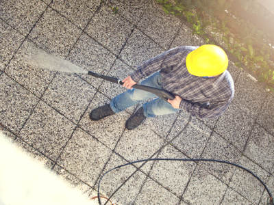 Person mit Schutzhelm reinigt Steinboden mit Hochdruckreiniger.
