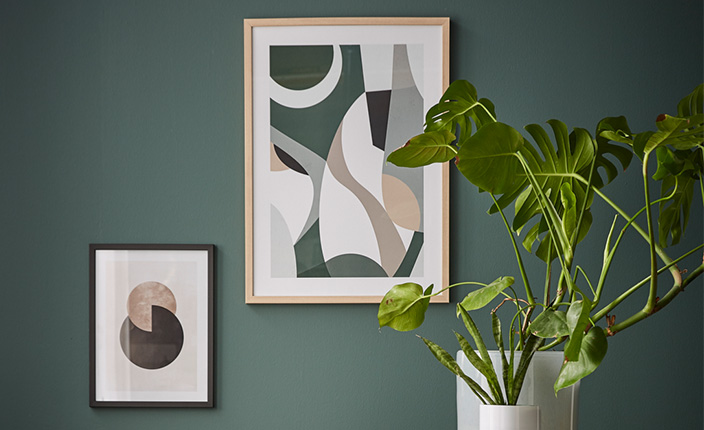 Zwei Zimmerpflanzen stehen vor einer Wand, die mit zwei Gemälden dekoriert ist