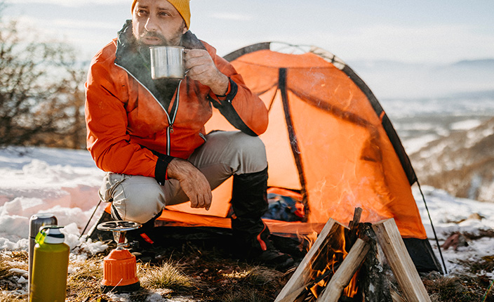 Mann sitzt vor Zelt im Schnee