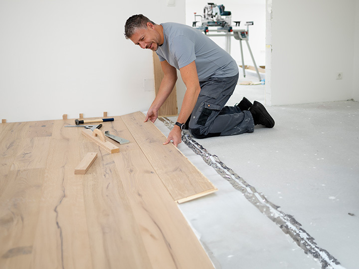 Mann der auf Baustelle im Haus Fußboden verlegt