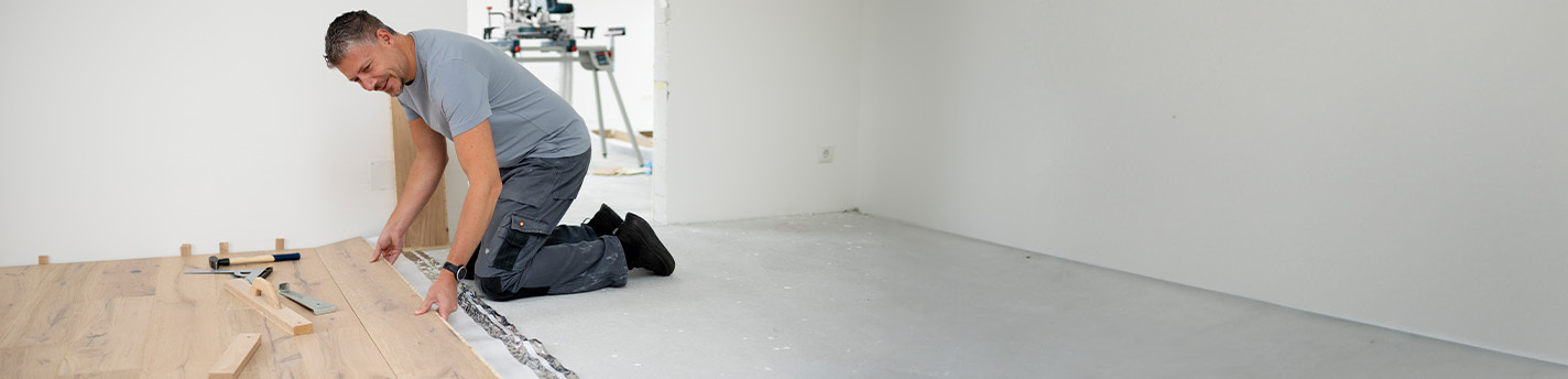 Mann der auf Baustelle im Haus Fußboden verlegt